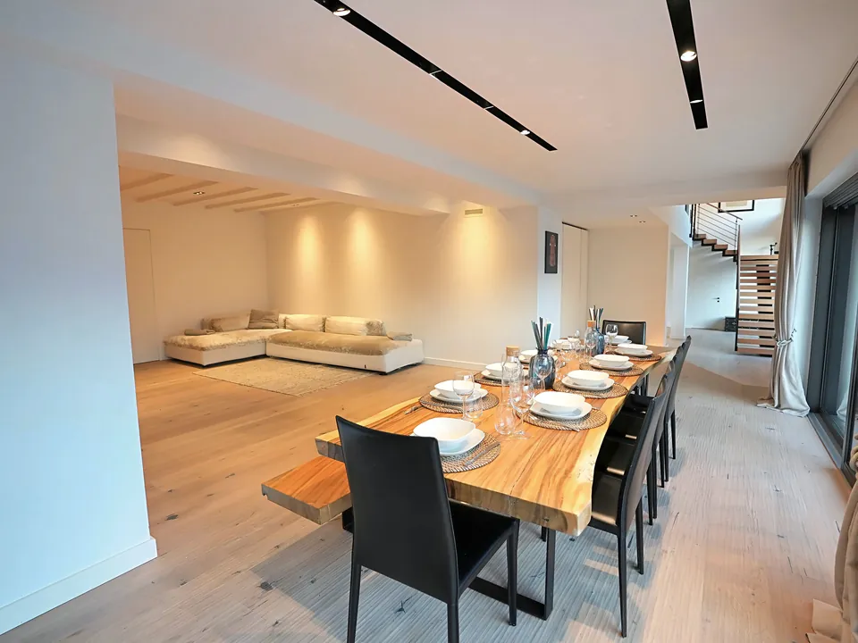 Open-plan dining and living area with long table and floating staircase behind