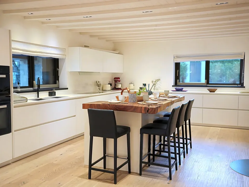 White kitchen with wooden-top island, black stools and windows