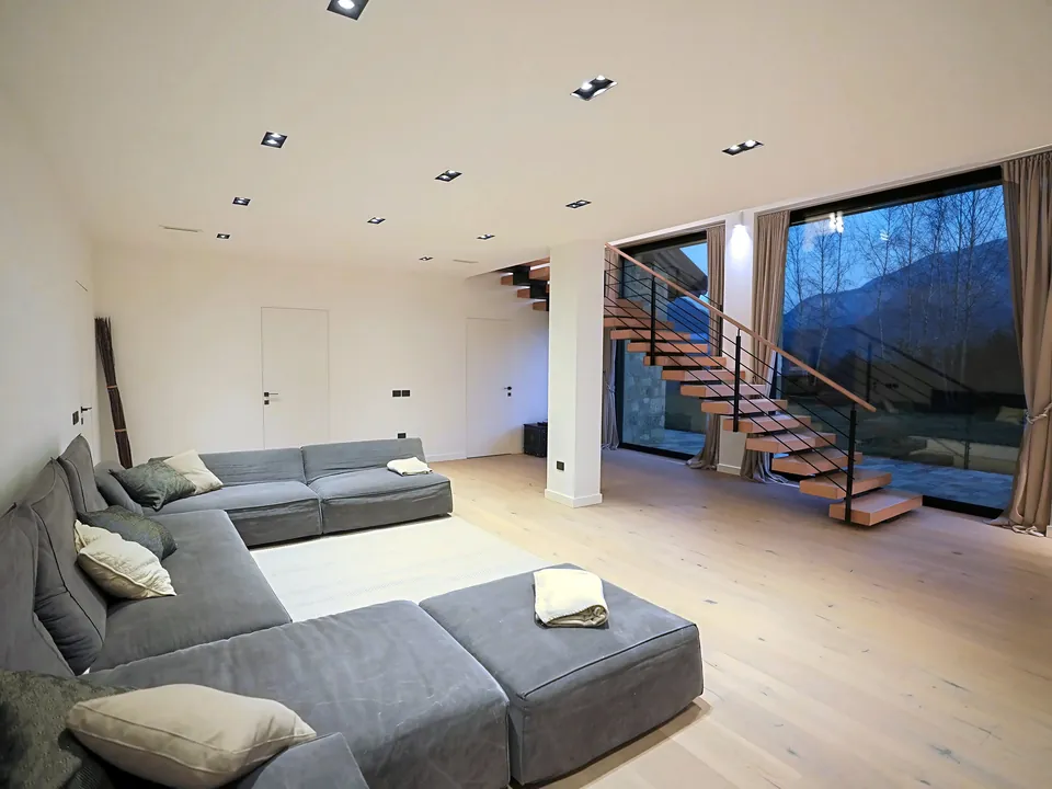 Living room with large grey sofa, floating staircase and glazing facing the mountain