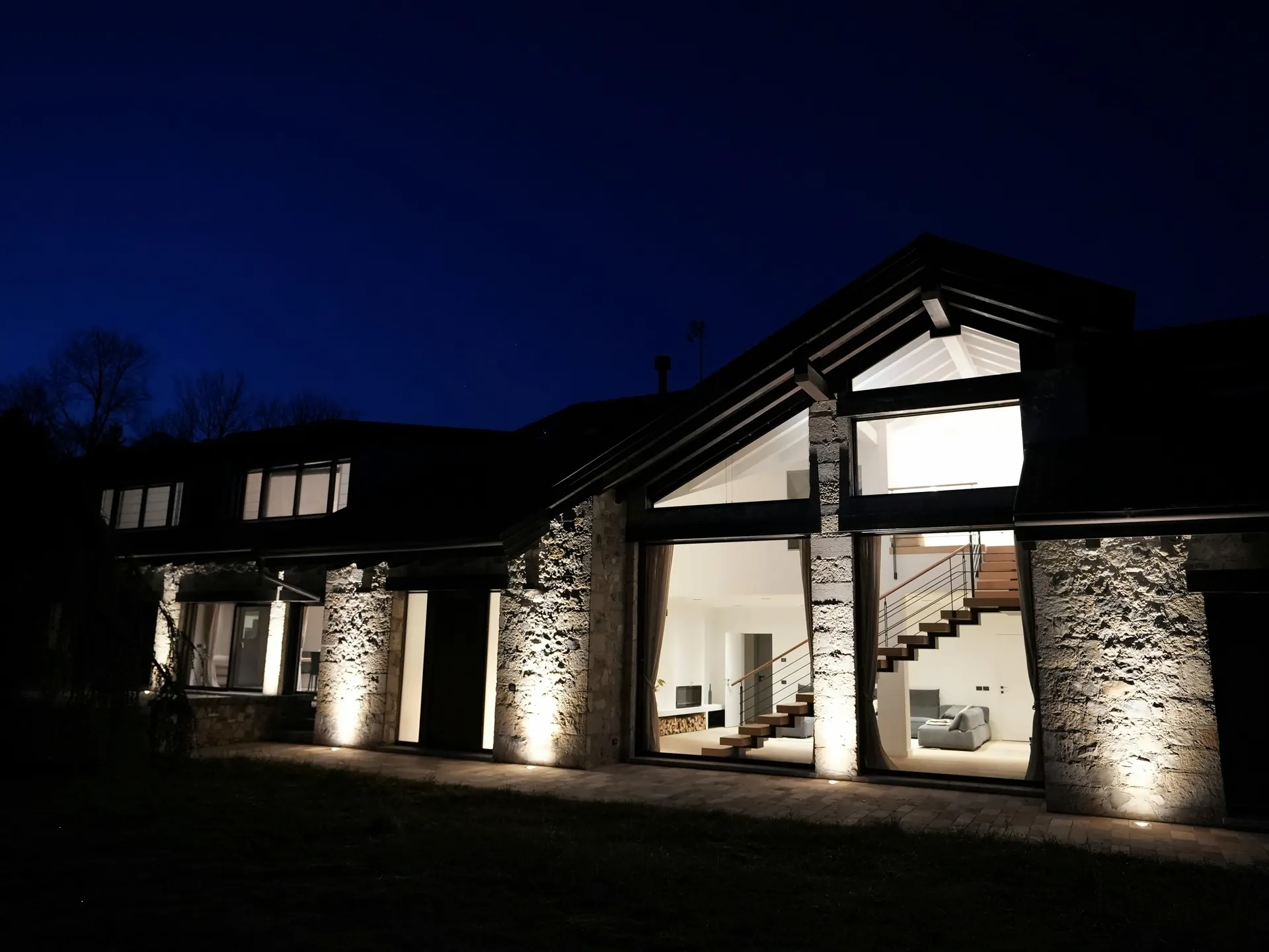 The house at night: lit stone facade and illuminated windows of the living room